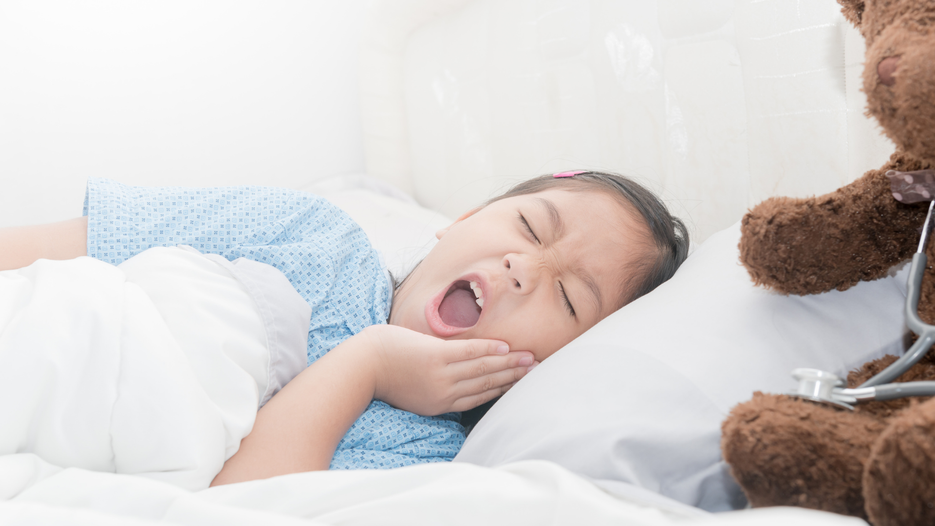 young girl in bed holding jaw in pain